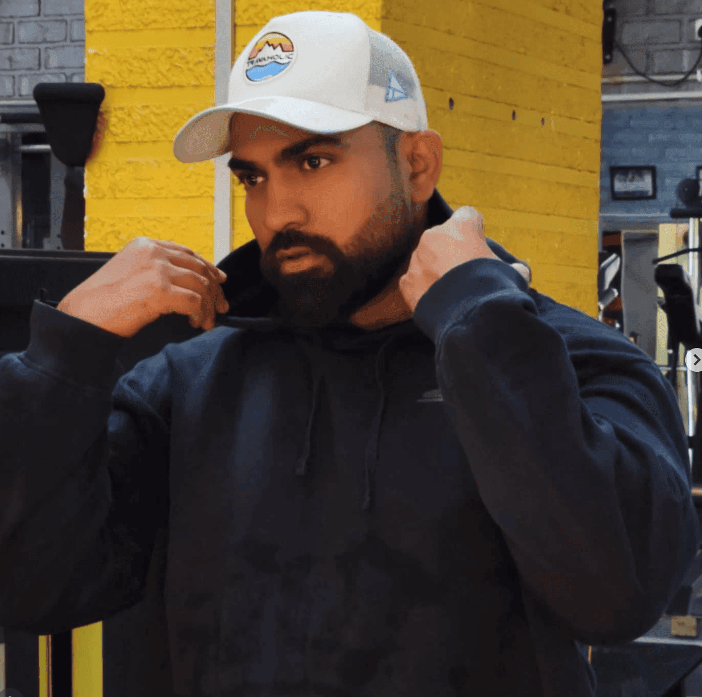 Golden hour on a city block, halfway through pulling a hoodie on — the cap doesn't come off either way.