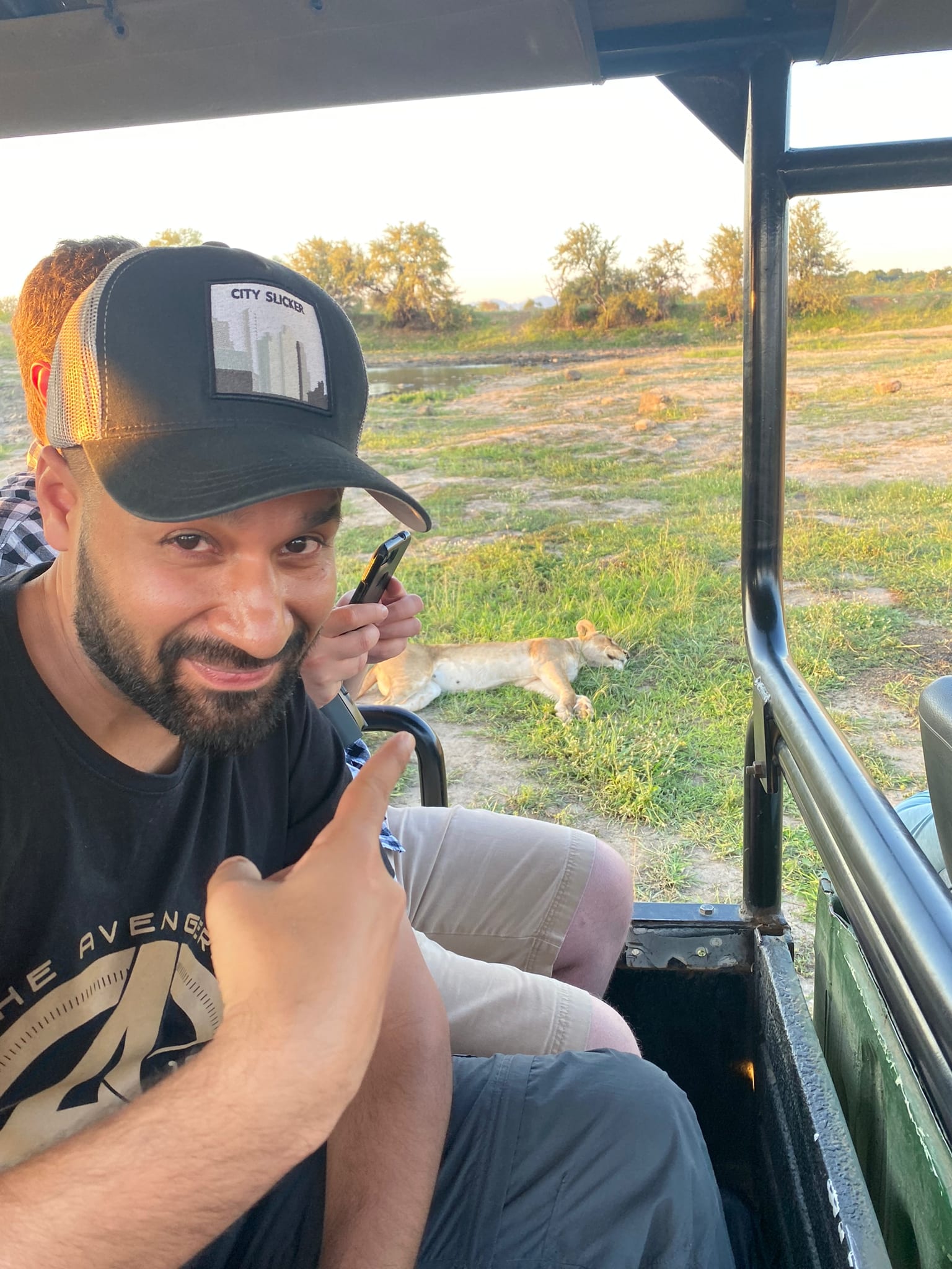 A lion asleep in the grass, a thumbs up from the jeep — priorities in order.